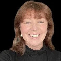 Portrait of a woman with reddish-brown hair smiling, wearing a black top and pearl earrings.