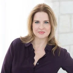 Portrait of a woman with shoulder-length blonde hair, wearing a dark purple top, against a white background.